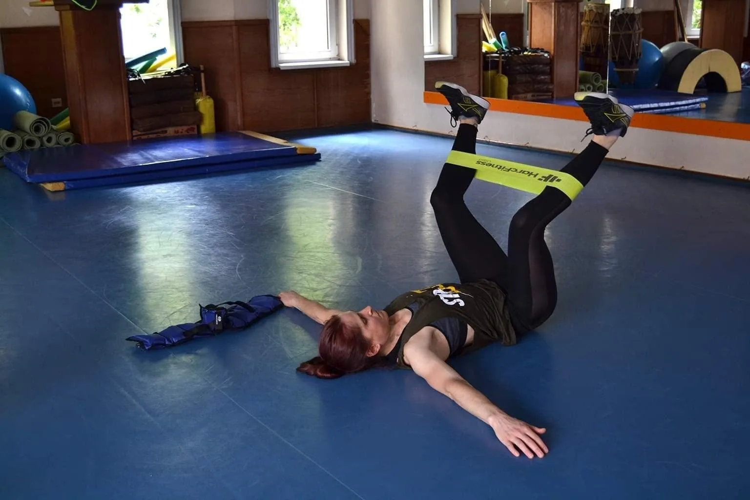 Jelena leži na podu sale i radi vežbu za noge sa elastičnom trakom.